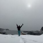 Person celebrating on snowy shore by water.