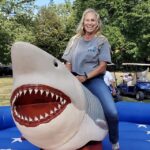 Woman riding mechanical shark outdoors, smiling.